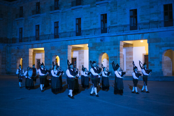 Banda de gaitas y percusión desfila durante una actuación nocturna en el patio de un edificio histórico iluminado en azul.