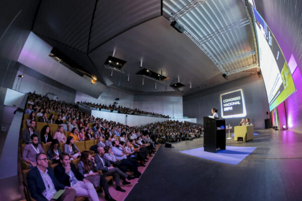 Vista general de un congreso nacional con el auditorio lleno de asistentes y una ponente interviniendo desde el escenario.