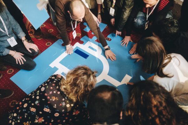 Participantes de una convención empresarial colaboran en una actividad de team building con piezas de un puzle gigante.